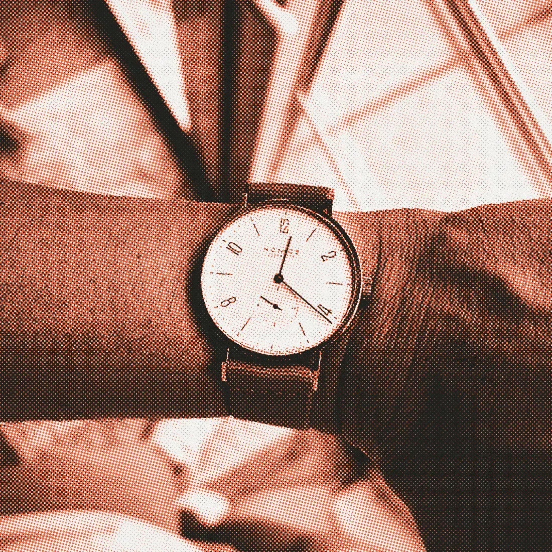 A Nomos Tangente with a white dial, a red 12 and a gray textile strap, on a wrist