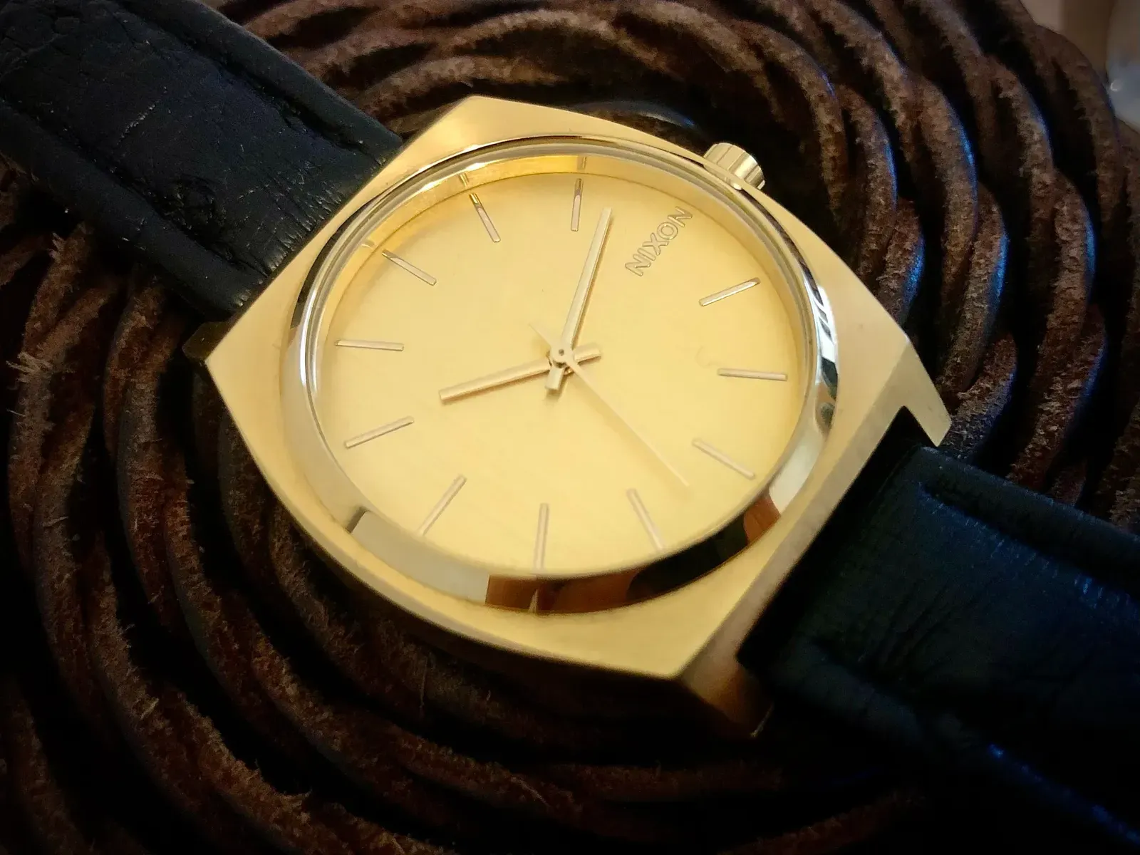 The Time Teller on a narrow black strap, resting on a coiled brown leather cord